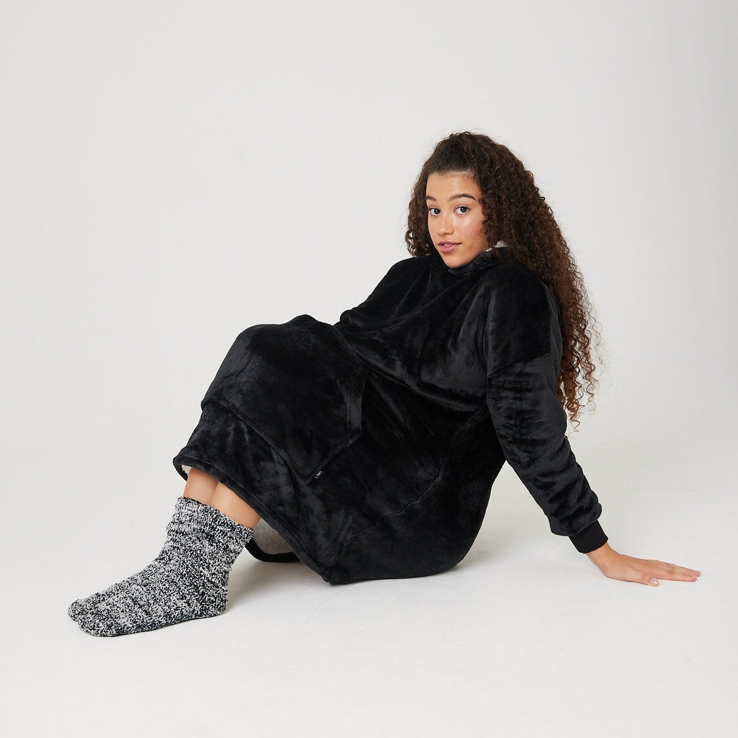 Black hooded blanket for kids sat down with oversized hoodie over knees